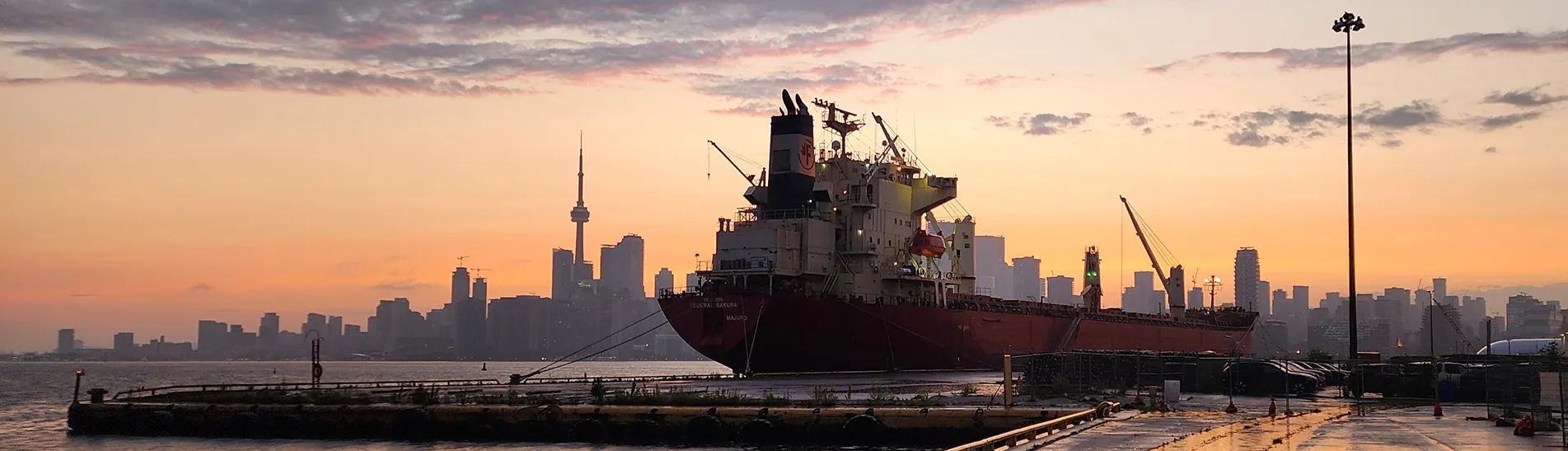 Sunset image of a ship at the port in the foreground and the Toronto skyline in the background.